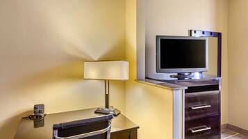 A hotel room with a desk, chair, lamp, television, and a minibar.