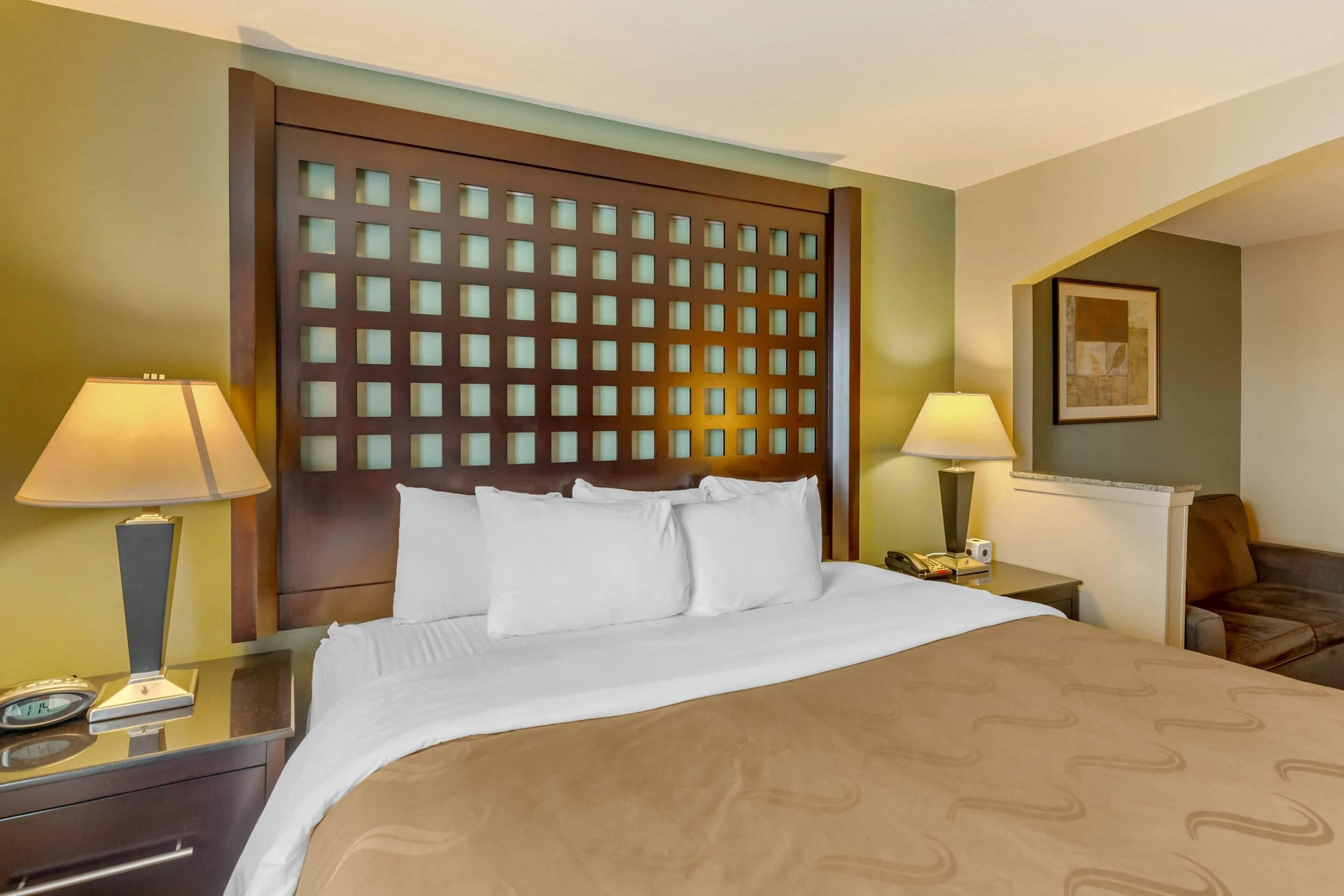A hotel room with a bed, bedside tables, lamps, a clock, and a painting on the wall.