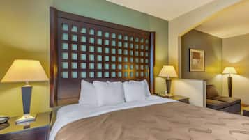 A hotel room with a large bed, two bedside tables, a nightstand, a wall-mounted lamp, and a framed picture.