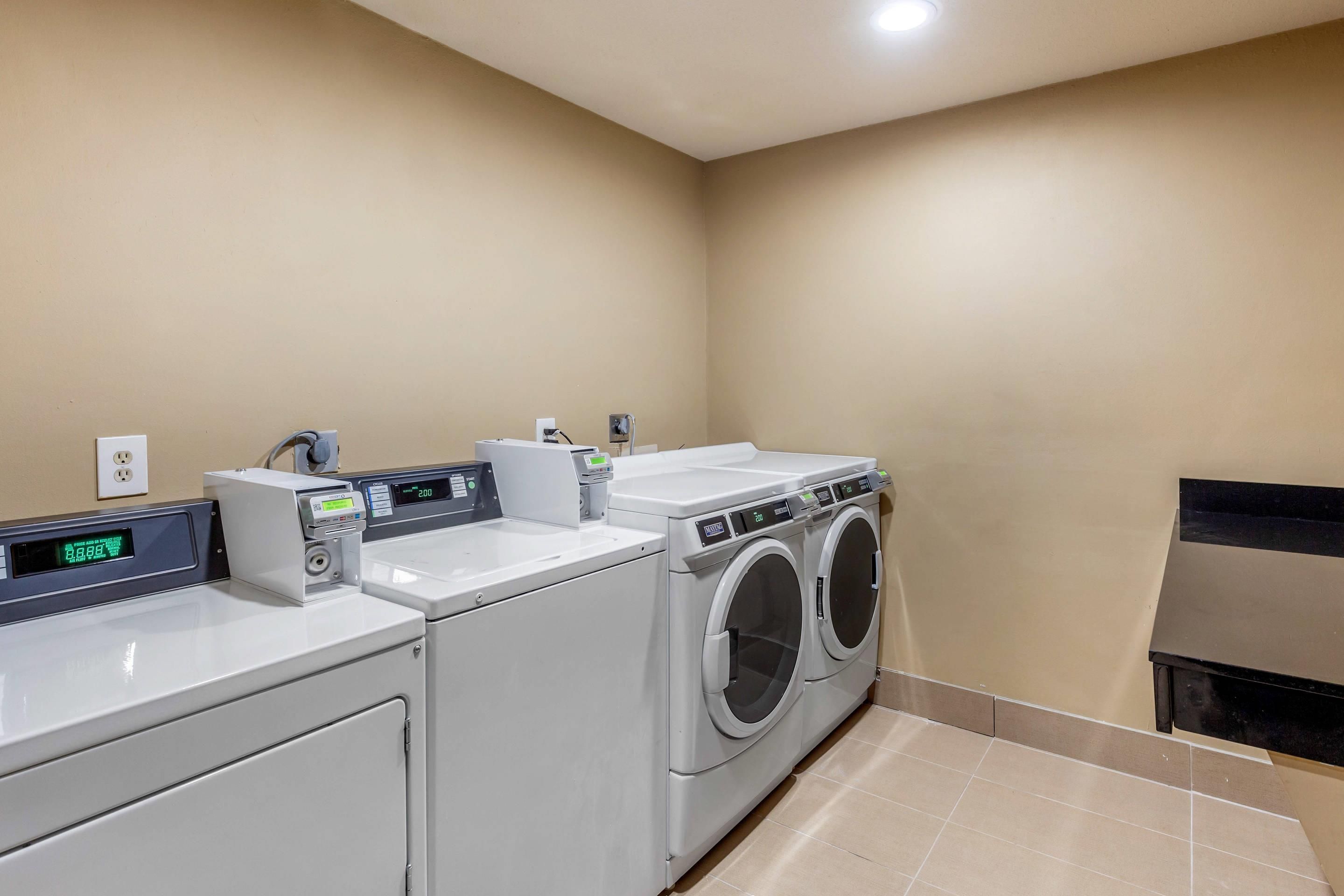 A laundry room with two washing machines and a dryer, a control panel, and a wall-mounted electrical outlet.