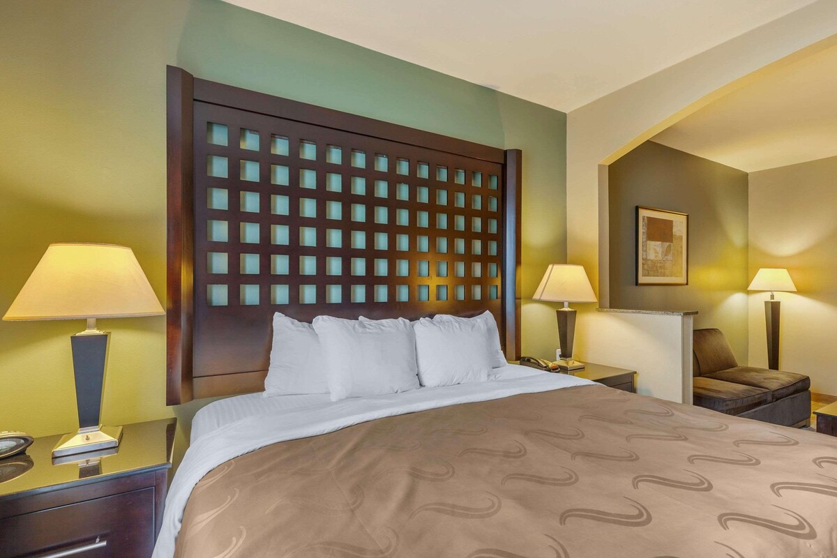 A hotel room with a large bed, two bedside lamps, a wooden headboard with a grid pattern, and a small painting on the wall.