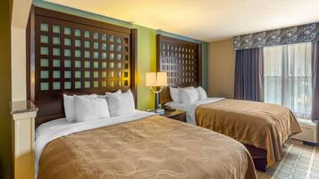 A hotel room with two beds, a nightstand, a lamp, and a window with curtains.