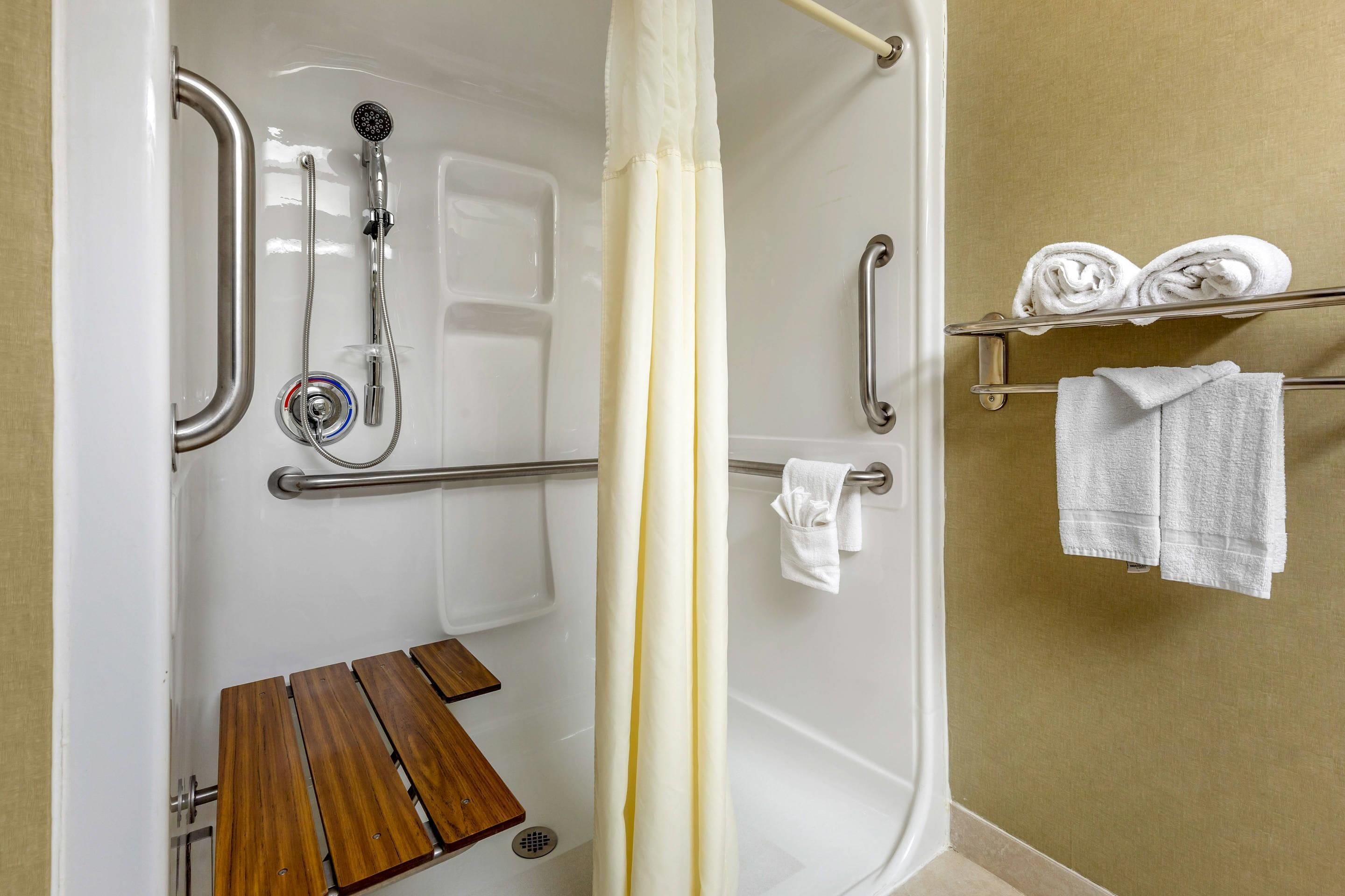 A shower area with grab bars, a wooden bench, and a towel rack with towels.