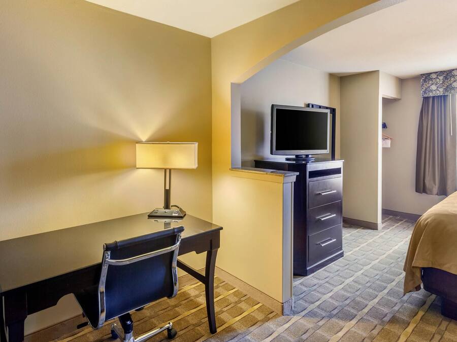A hotel room with a desk, chair, television, and a bed.