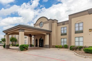 A modern building with a covered entrance, multiple windows, and a parking lot. - Quality Suites Sherman (Sherman)