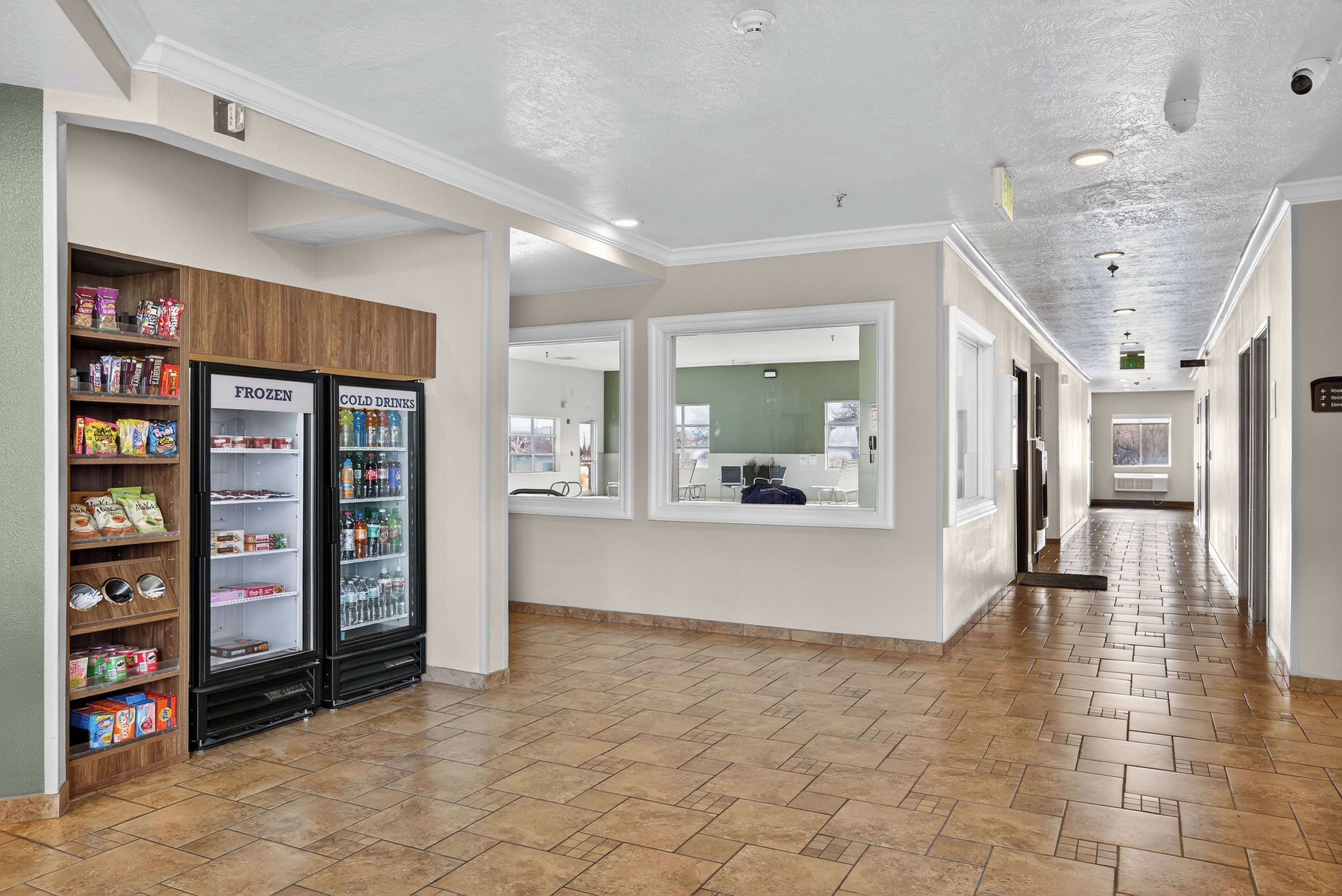 A hallway with a tiled floor, a snack bar with frozen and cold drink refrigerators, and a window with a view of the outside.
