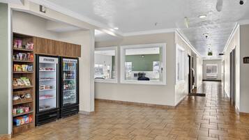 A hallway with a tiled floor, a snack bar with frozen and cold drink refrigerators, and a window with a view of the outside.