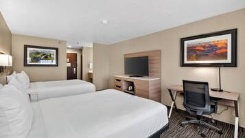 A hotel room with two beds, a desk with a computer, a TV, and framed pictures on the walls.
