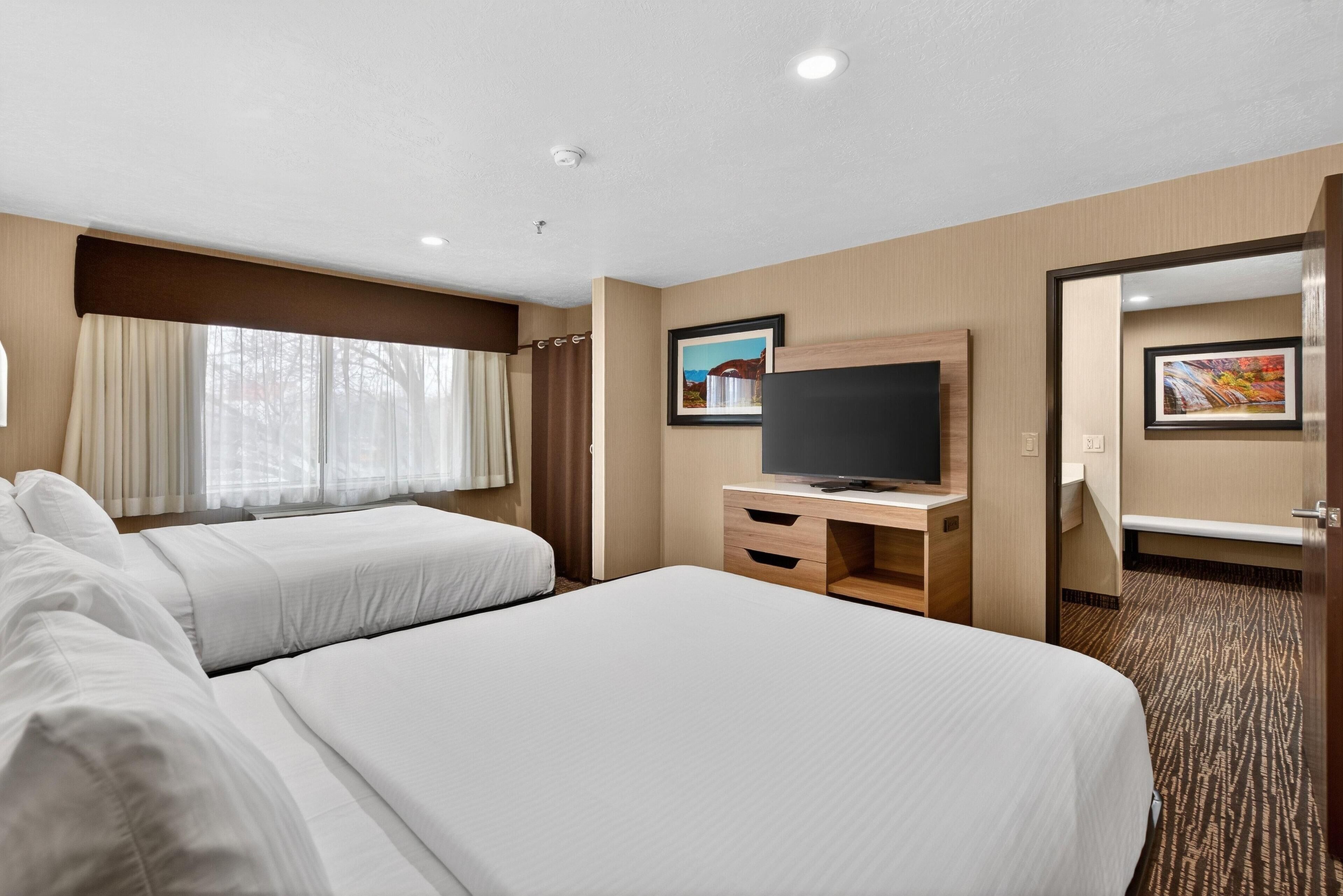 Une chambre d’hôtel avec deux lits, une télévision, un bureau et une salle de bain visible à travers une porte ouverte.