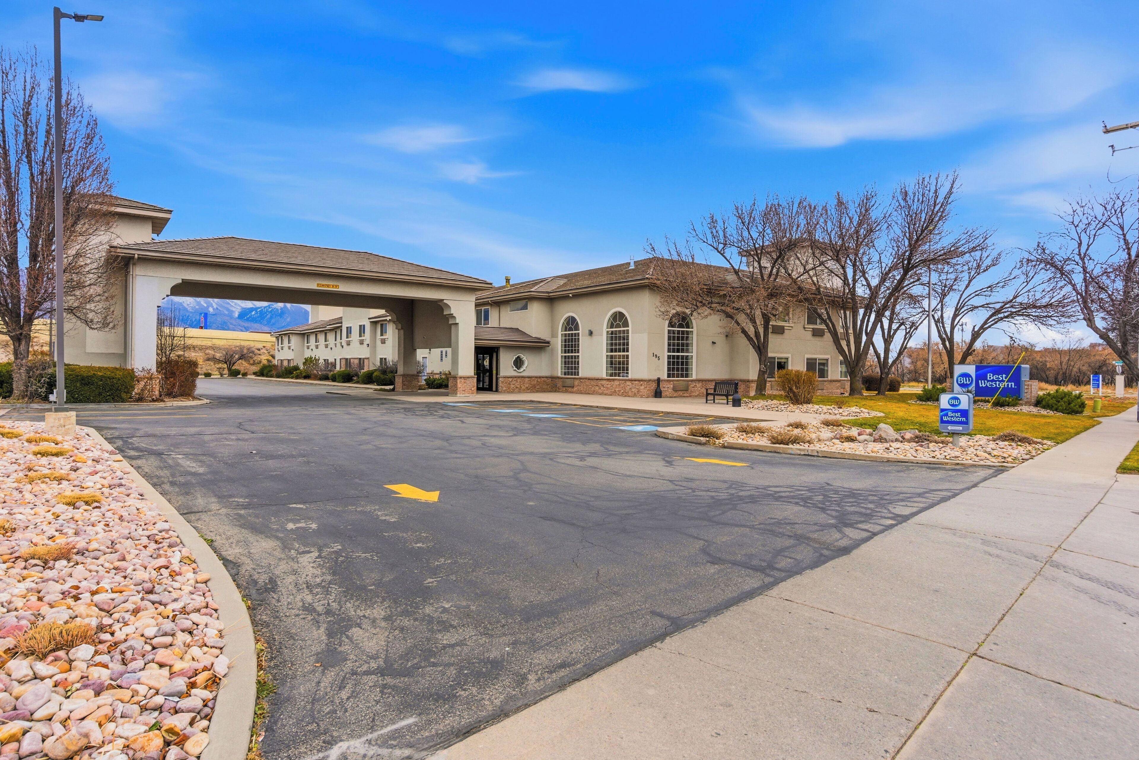 A building with a covered entrance, a parking lot, and a sign indicating 'Best Western' hotel.