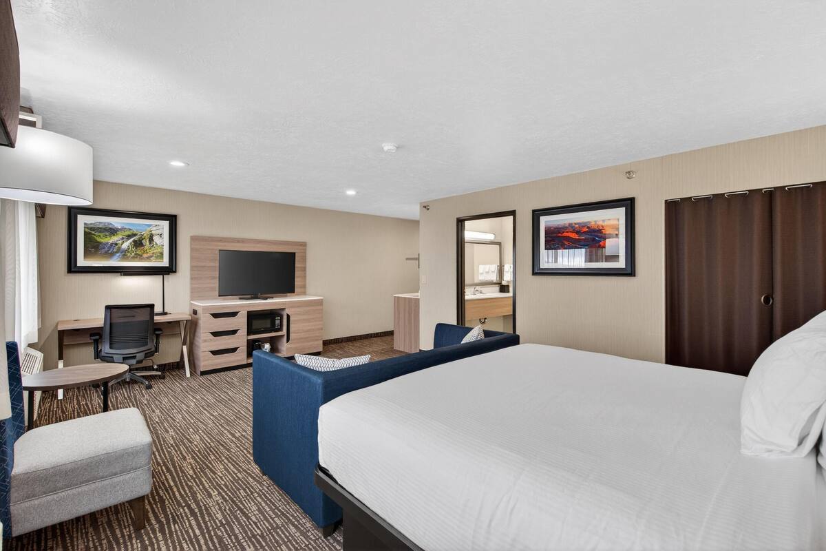 A hotel room with a large bed, a desk with a chair, a television, a small table, and a sofa.