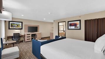 A hotel room with a large bed, a desk with a chair, a television, a small table, and a sofa.