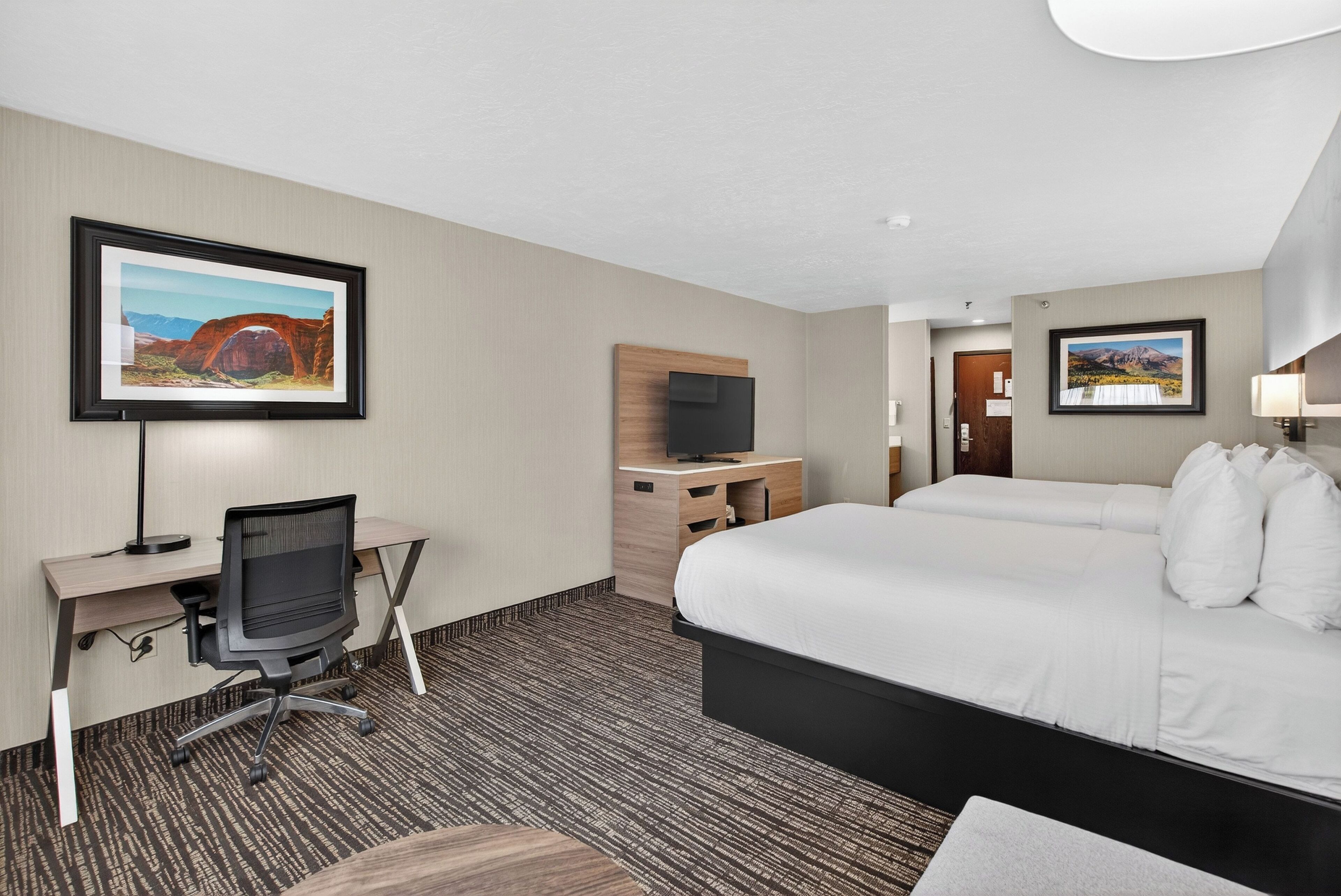 Habitación de hotel con cama, escritorio, silla, televisor y obras de arte en las paredes.