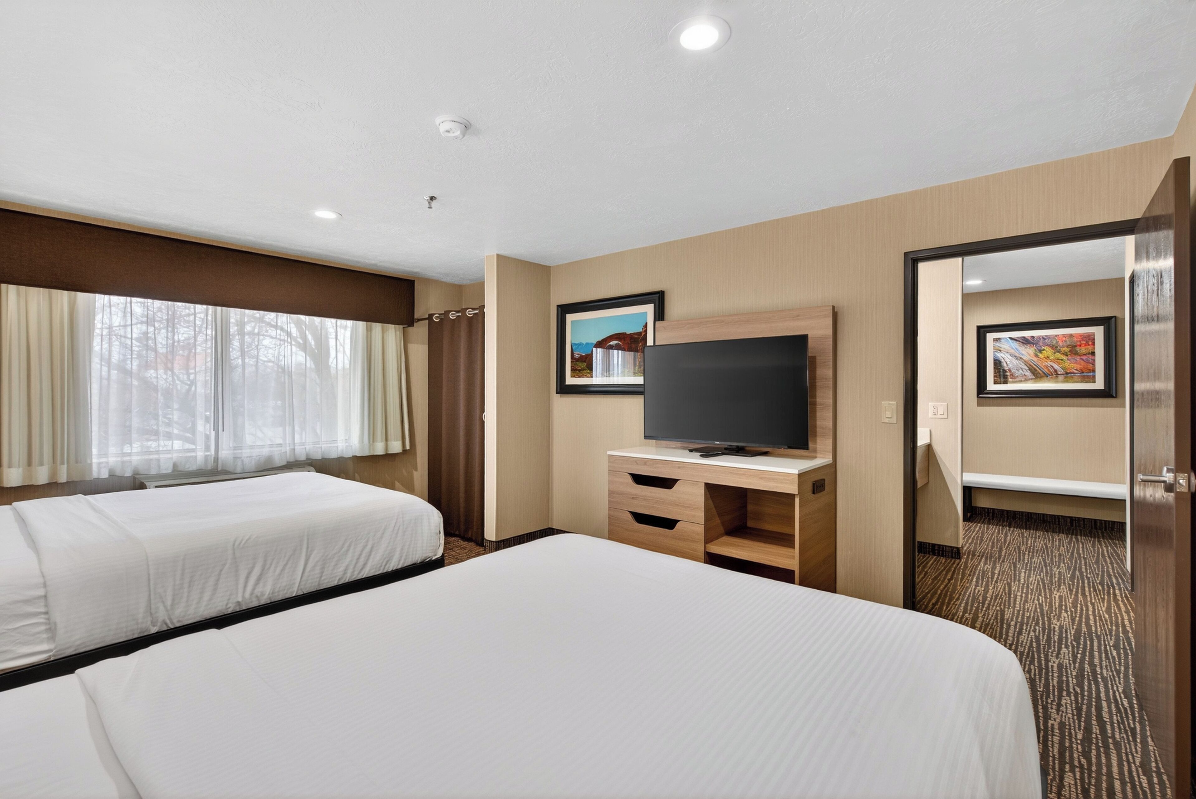 Habitación de hotel con dos camas, televisión, escritorio y espejo.