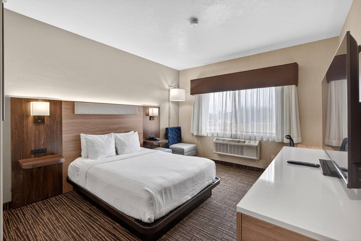 A hotel room with a bed, bedside tables, a desk, a lamp, and a window with curtains.