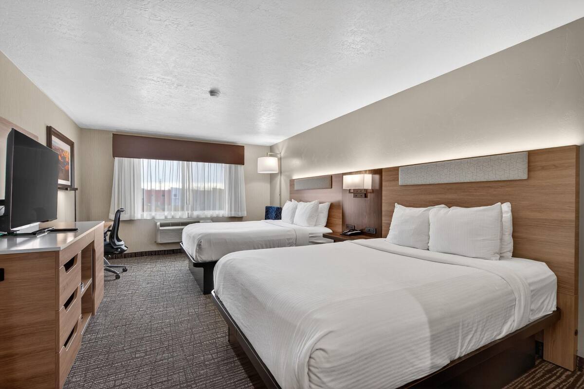 A hotel room with two beds, a desk, a TV, and a window with curtains.