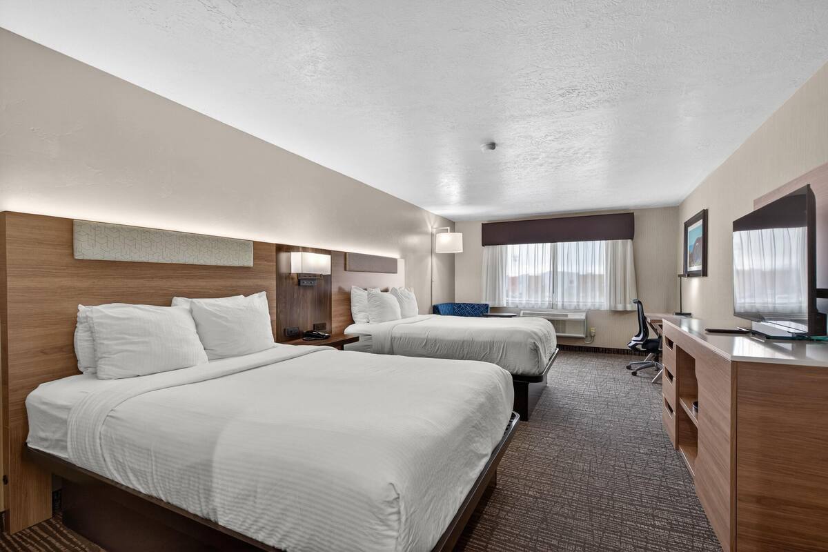 A hotel room with two beds, a desk, a chair, a TV, and a window with curtains.