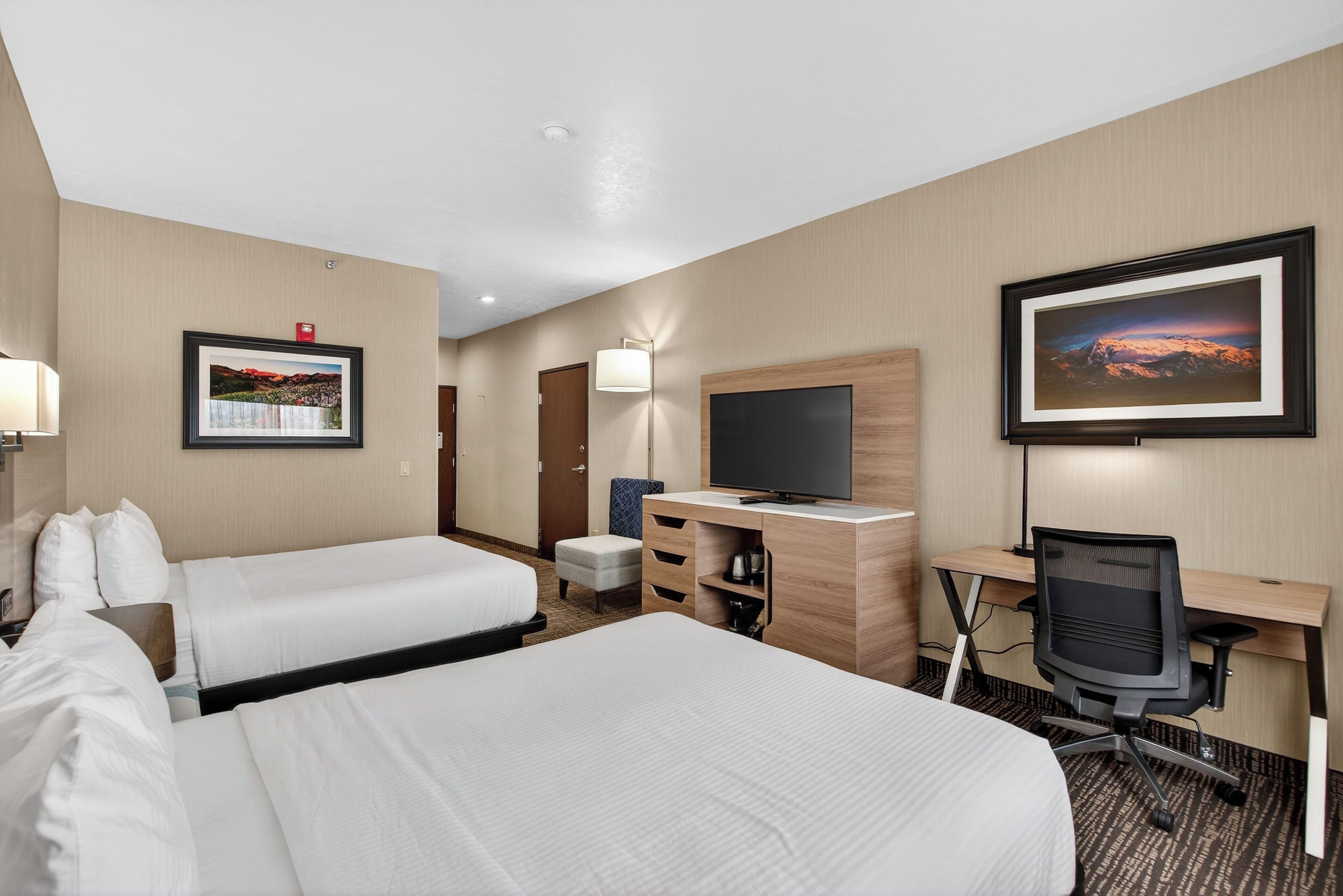 A hotel room with two beds, a desk, a chair, a TV, and a wall-mounted picture.