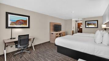 Habitación de hotel con cama, escritorio, silla, televisor y obras de arte en las paredes.