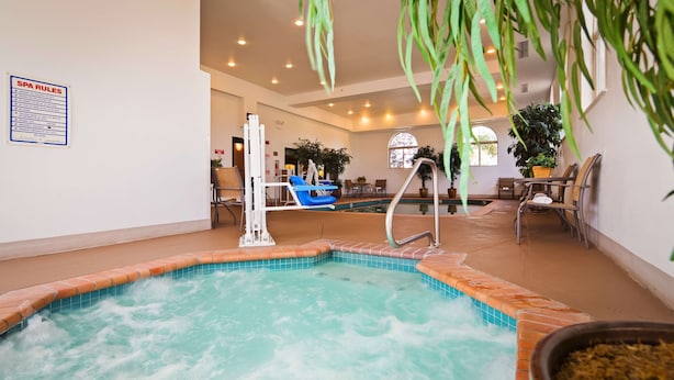 An indoor swimming pool with a water fountain feature, surrounded by lounge chairs and potted plants.