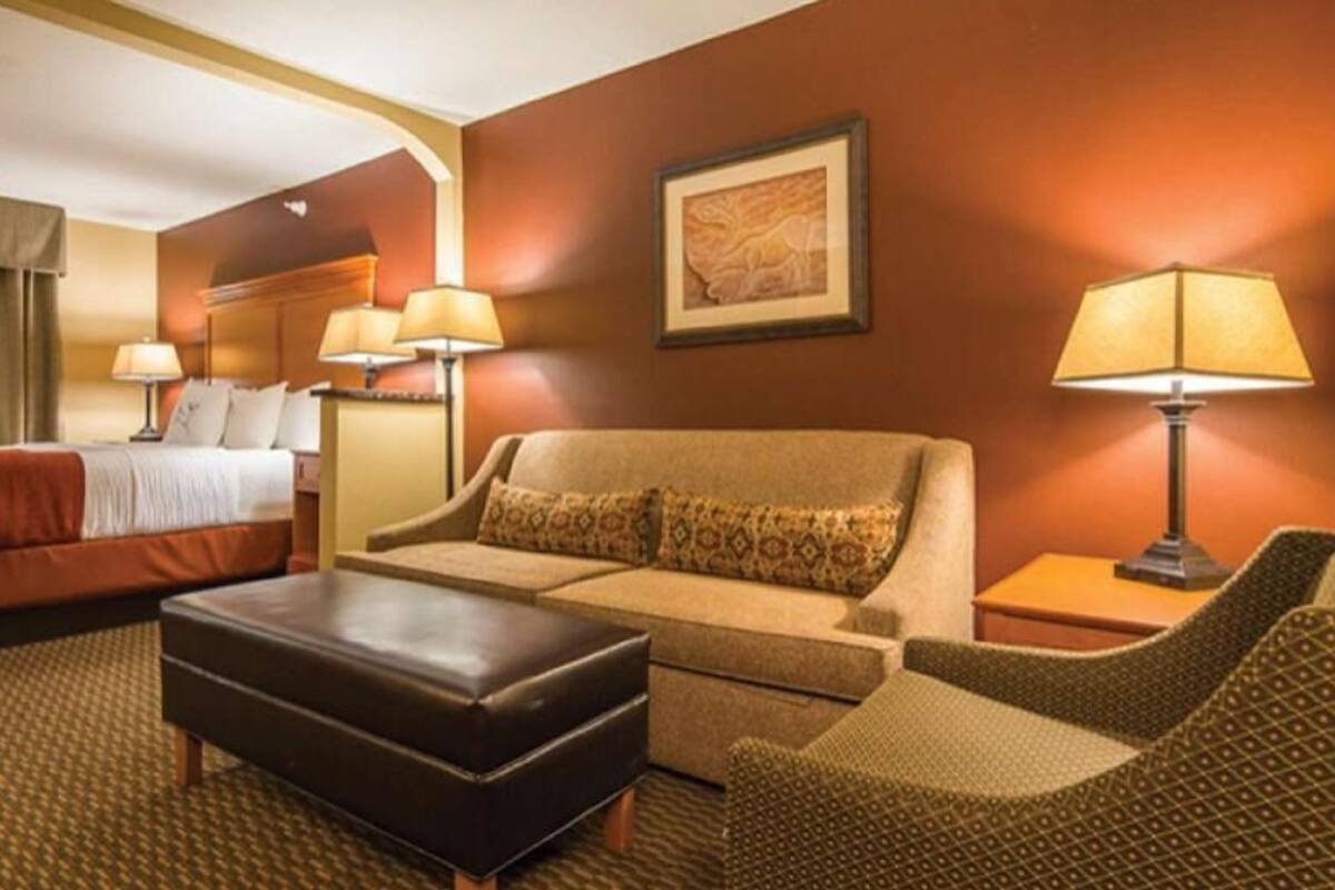 Una habitación de hotel con cama, sofá, sillón, mesa y dos lámparas.