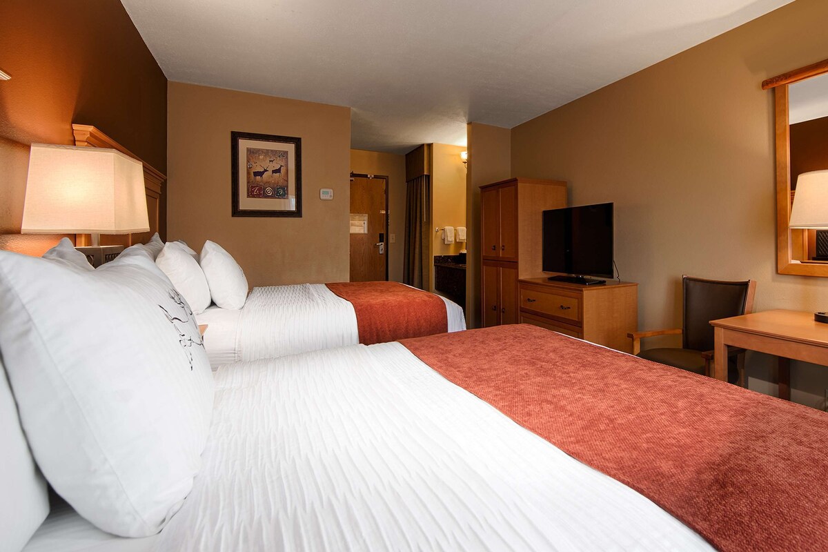 Ein Hotelzimmer mit zwei Betten, einem Schreibtisch, einem Fernseher und einem im Hintergrund sichtbaren Badezimmer.