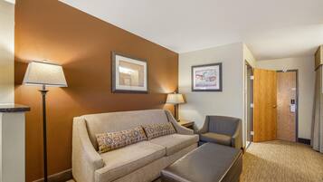 Une chambre d’hôtel avec un canapé, un fauteuil et une petite table. Il y a deux tableaux encadrés au mur, une lampe et une porte.