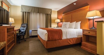 A hotel room with a bed, a desk, a chair, a TV, and two lamps.