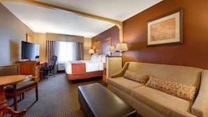 A hotel room with a bed, a sofa, a desk with a chair, a television, and a framed picture on the wall.