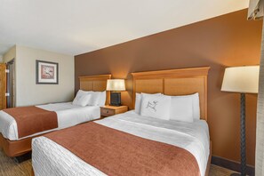 Een hotelkamer met twee bedden, een nachtkastje met een lamp, een lijst met een foto aan de muur en een deur.