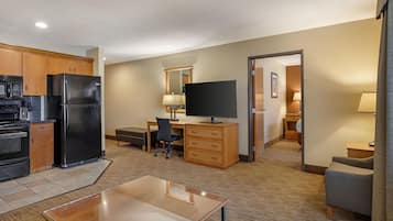 A compact hotel room with a kitchenette, a flat-screen TV, a desk, and a seating area.