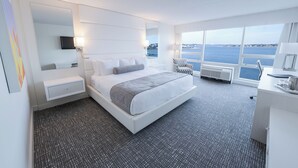 A modern hotel room with a large bed, a desk, and a view of the sea.