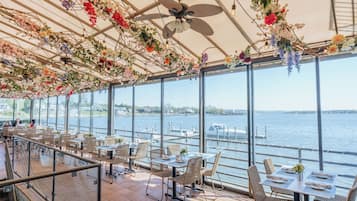 Enjoy meals with a view of the water from this dining area, featuring wicker furniture and a ceiling fan.