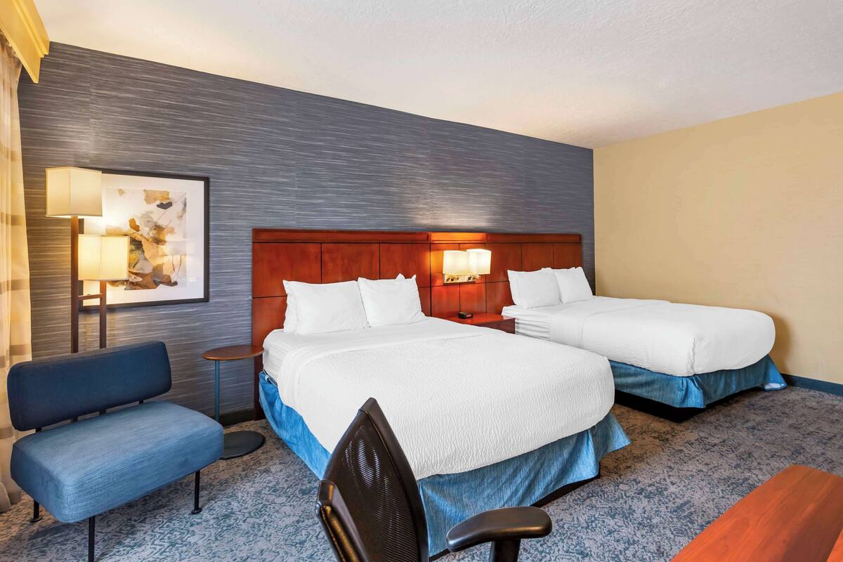 Une chambre d’hôtel avec deux lits, un bureau, une chaise et une lampe.