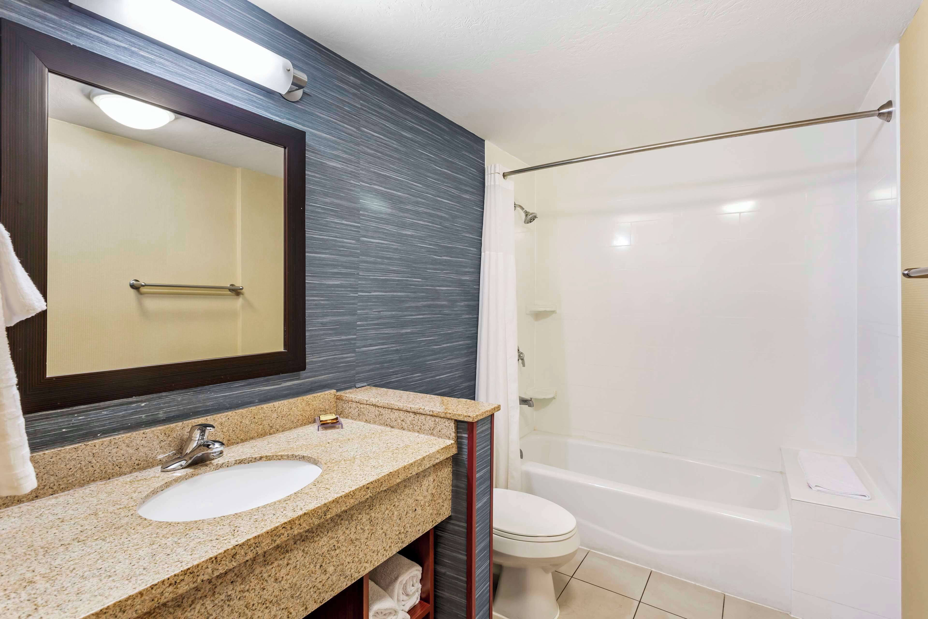 A bathroom with a granite countertop sink, a mirror, a toilet, and a bathtub.