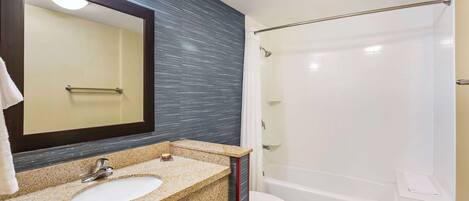 Un baño con lavamanos de encimera de granito, un espejo, inodoro y bañera.