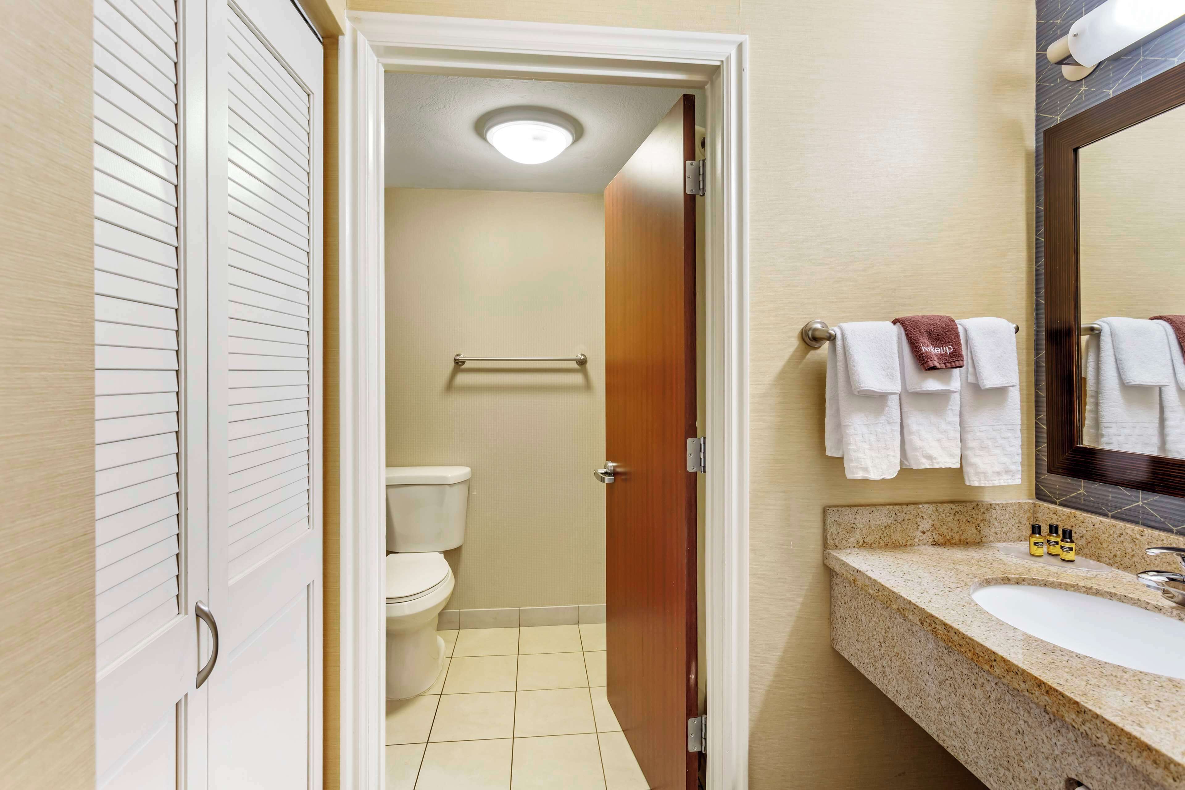 A bathroom with a toilet, a sink with a mirror, and towels on the wall.