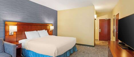 Habitación de hotel con cama, mesita de noche, lámpara, televisor y escritorio con silla.