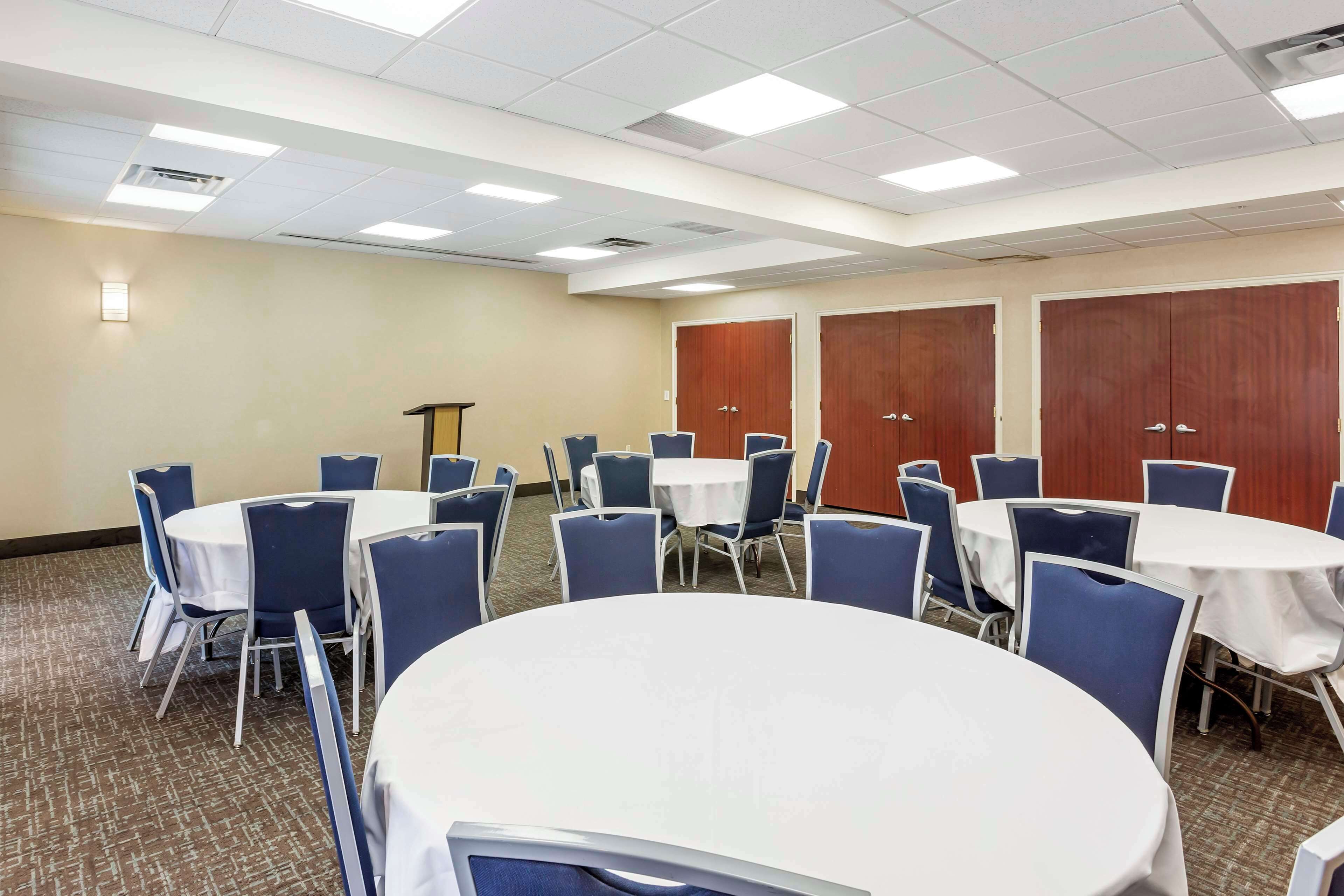 A conference room with round tables and blue chairs, equipped with ceiling lights and wooden doors.