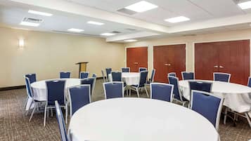 Une salle de conférence dotée de tables rondes et de chaises bleues, équipée de luminaires au plafond et de portes en bois.