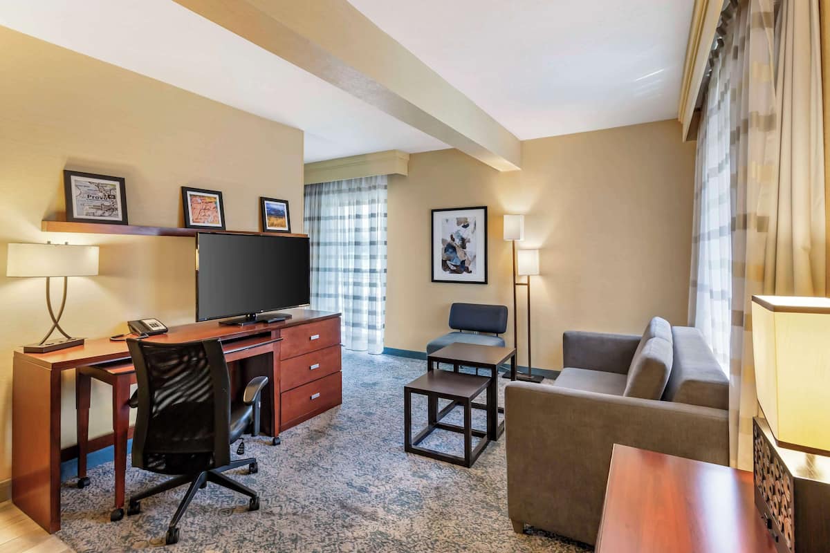 Une chambre d’hôtel avec un bureau en bois, une télévision, un canapé, une petite table et une lampe.