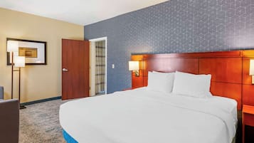 A hotel room with a large bed, a wooden headboard, two bedside lamps, a framed picture on the wall, and a carpeted floor.