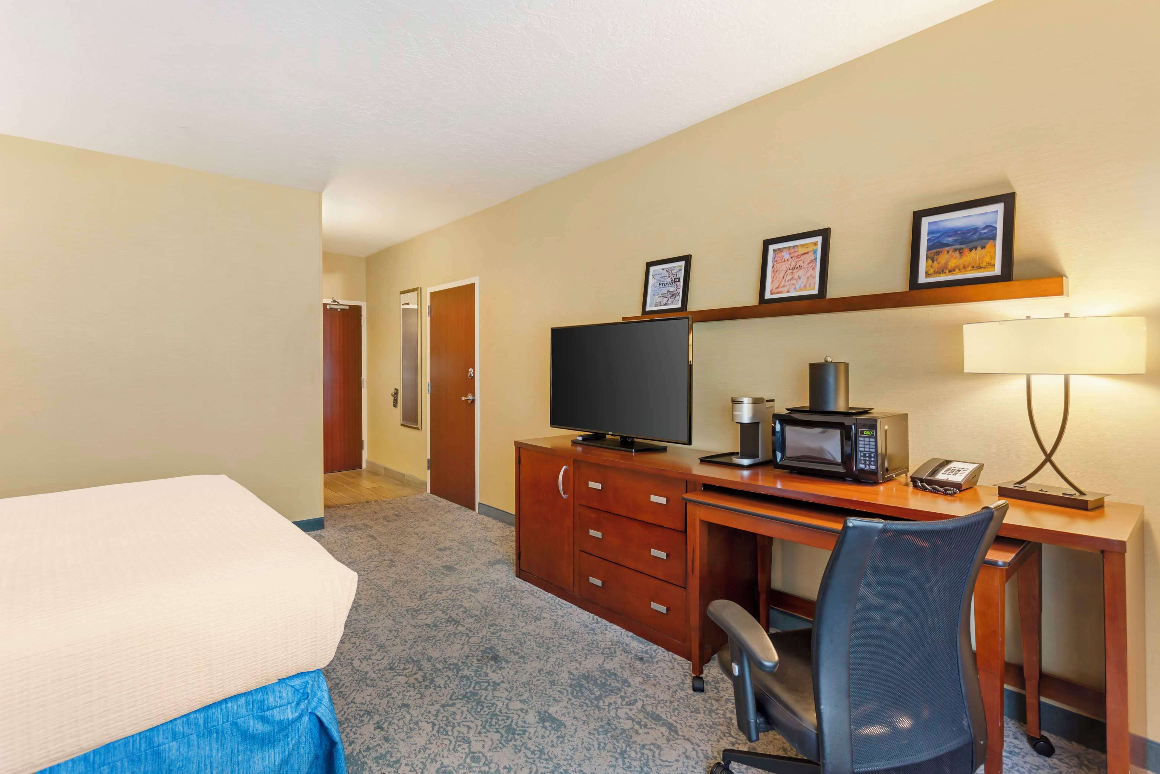 A hotel room with a bed, a desk with a computer, a microwave, and a telephone.