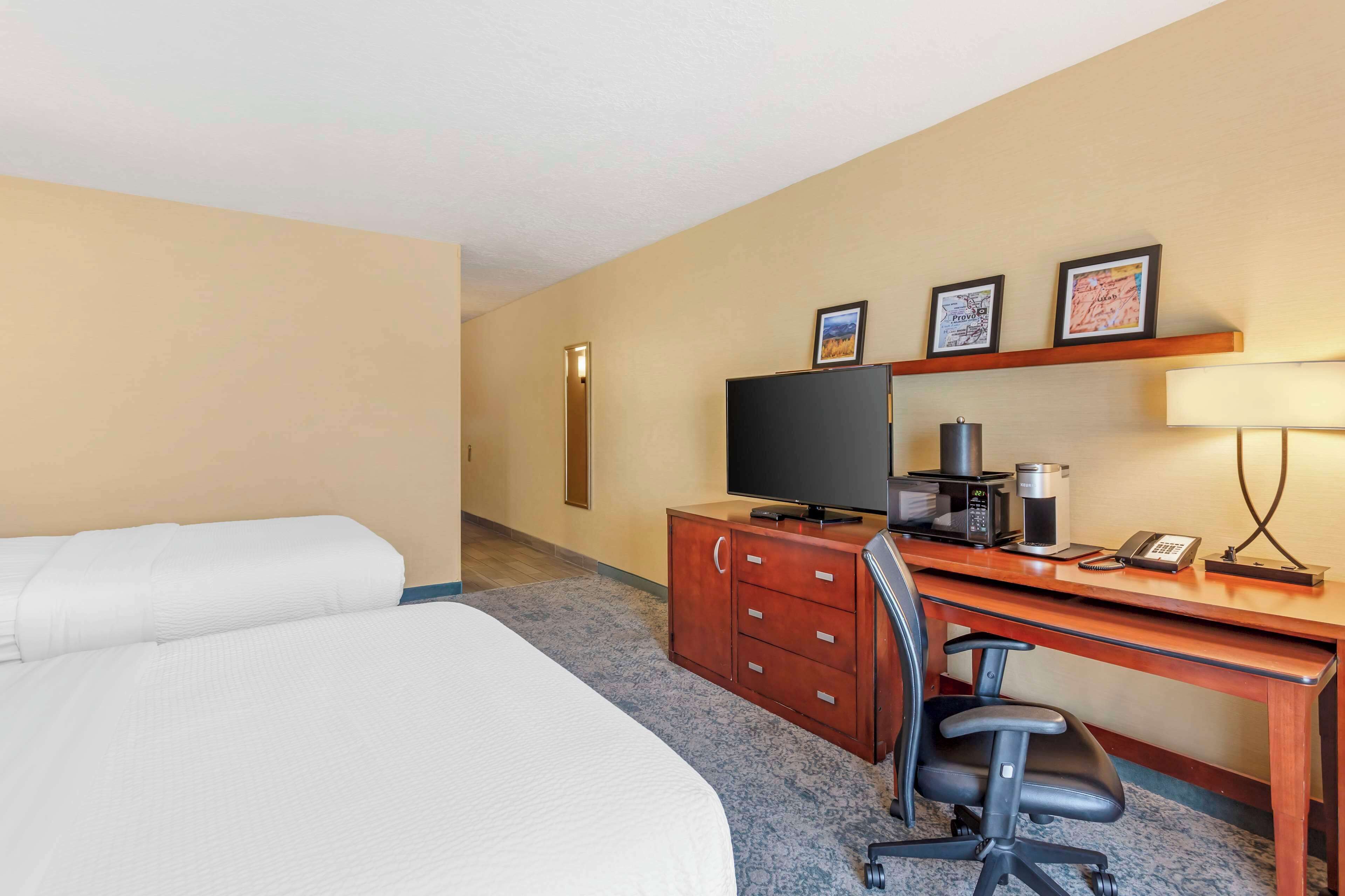 A hotel room with a bed, a desk with a computer, a TV, and a coffee maker.