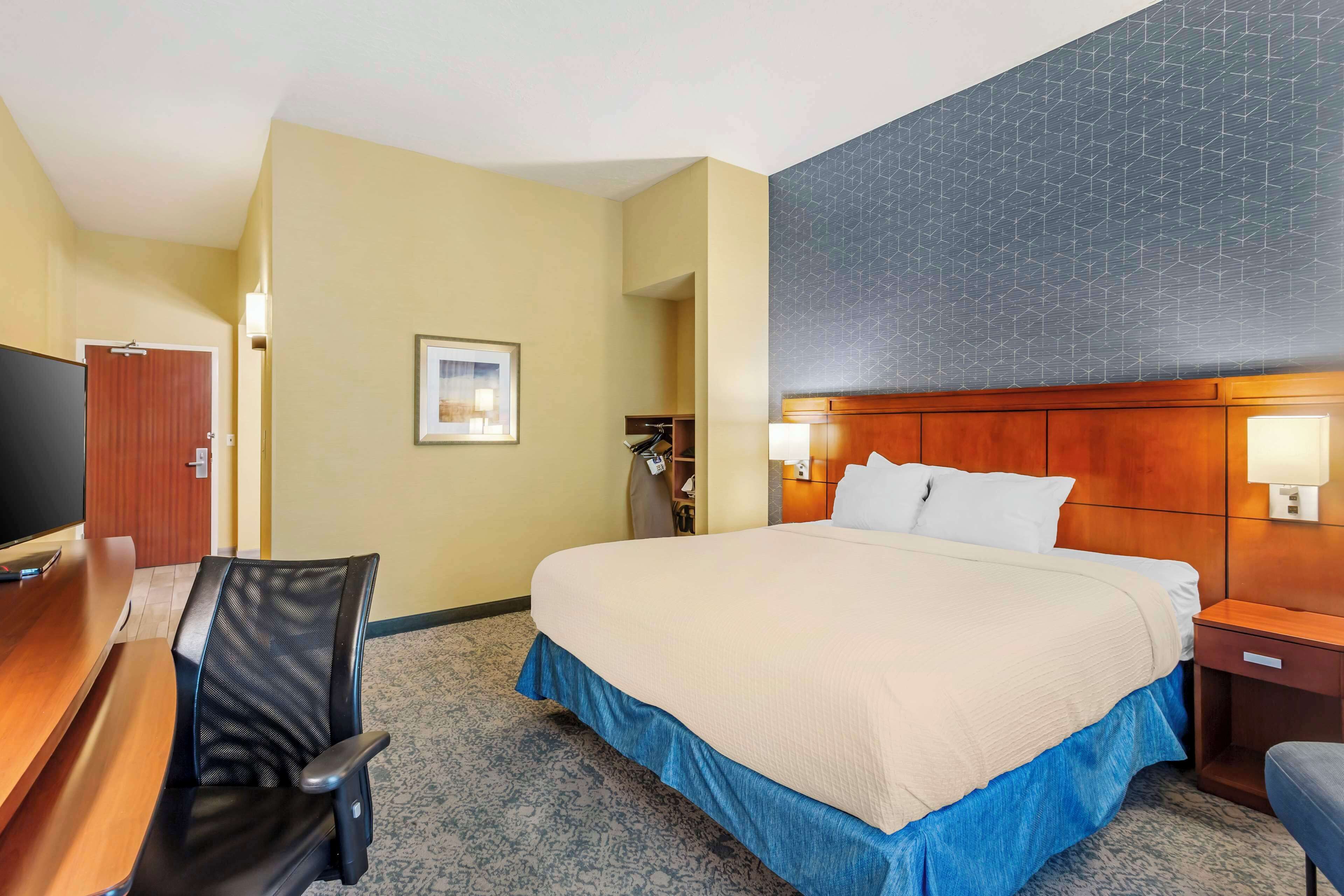 A hotel room with a bed, a desk, a chair, a television, and a wardrobe.