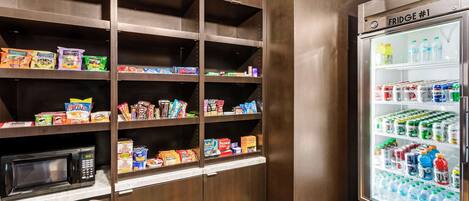 Una kitchenette con microondas, tres dispensadores de bebidas y un refrigerador lleno de bebidas y aperitivos.