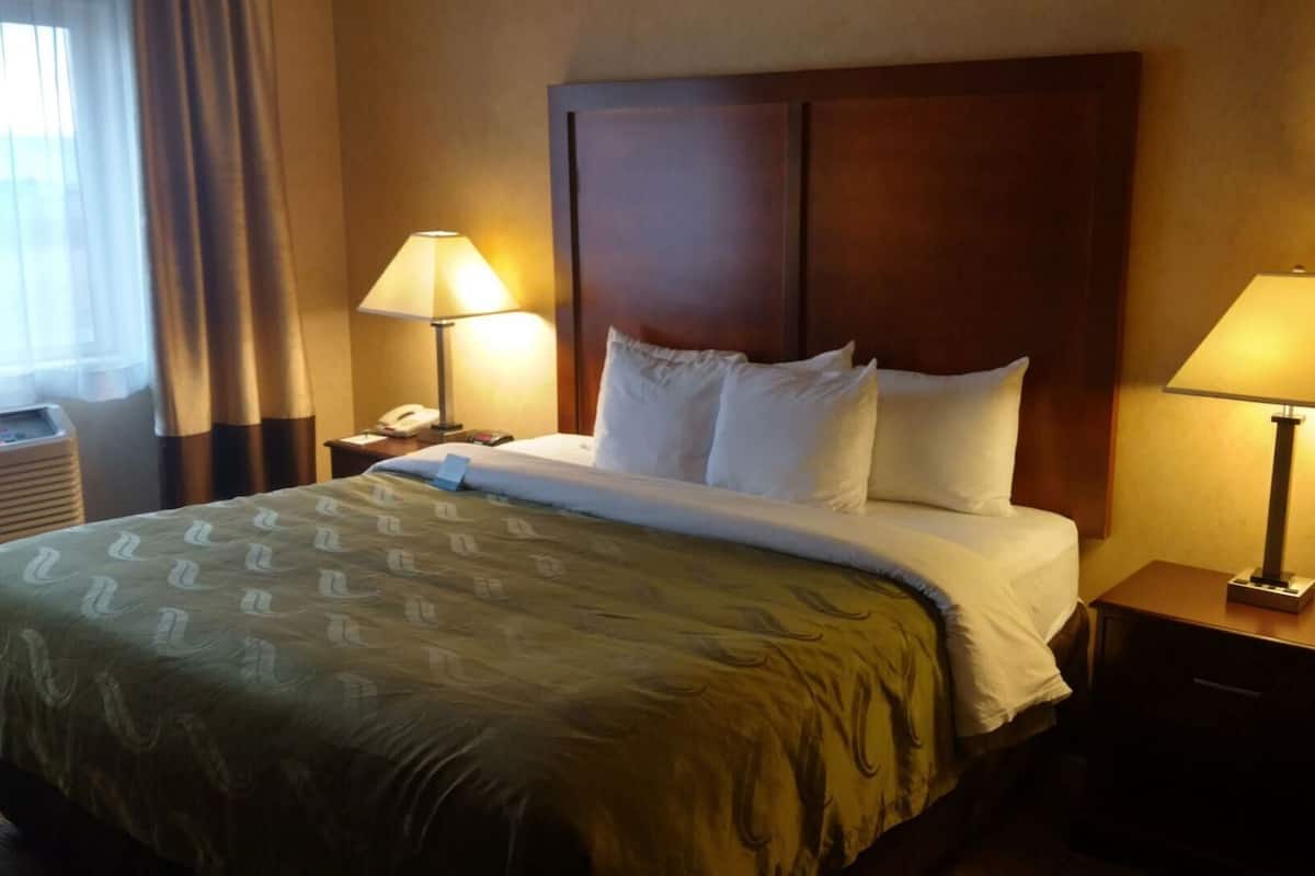 A hotel room with a large bed, two bedside lamps, a wooden headboard, and a nightstand with a phone.