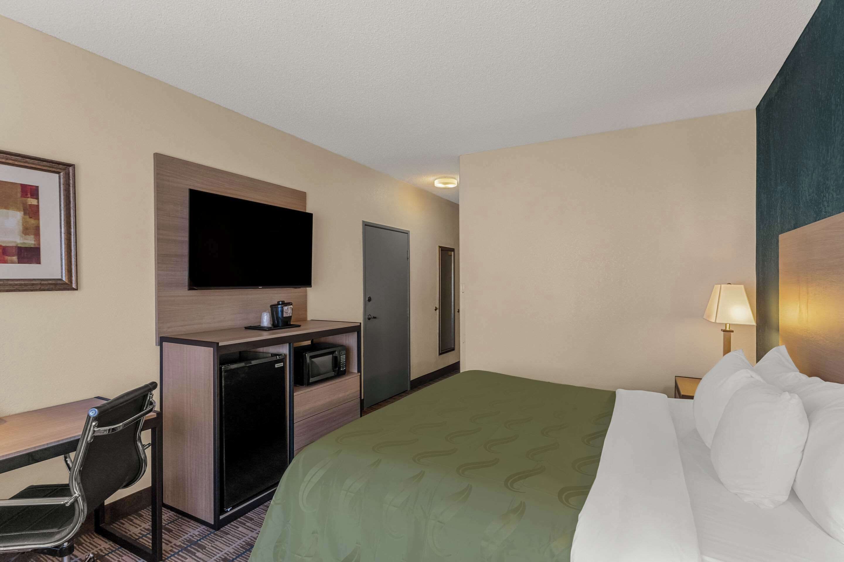 A hotel room with a bed, a desk with a computer, a microwave, and a television.