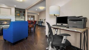 Una habitación de hotel con chimenea, un escritorio con impresora, un sillón azul y un área de comedor con mesa y sillas.