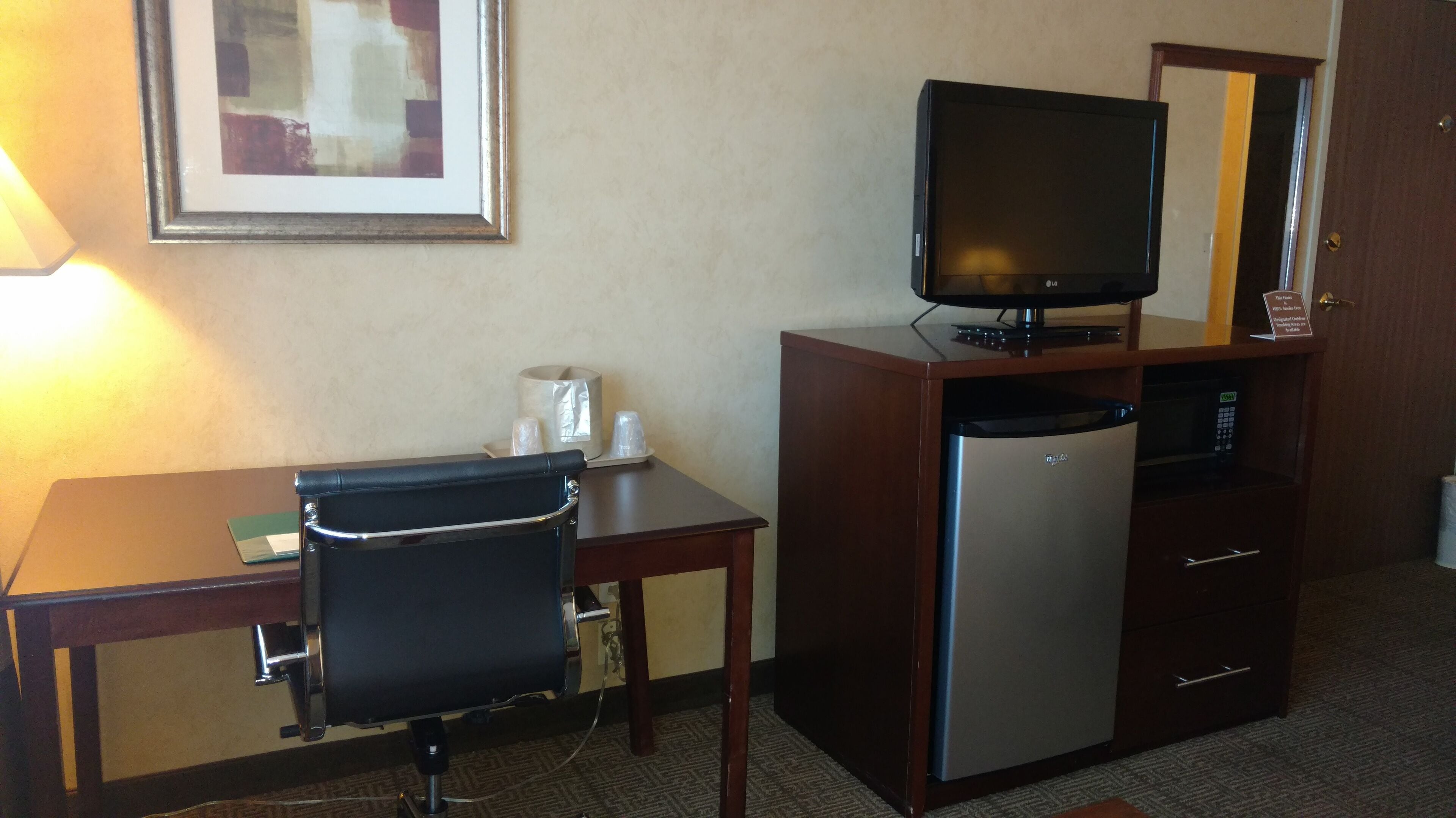 Una habitación de hotel con escritorio, silla, televisor, refrigerador y espejo.